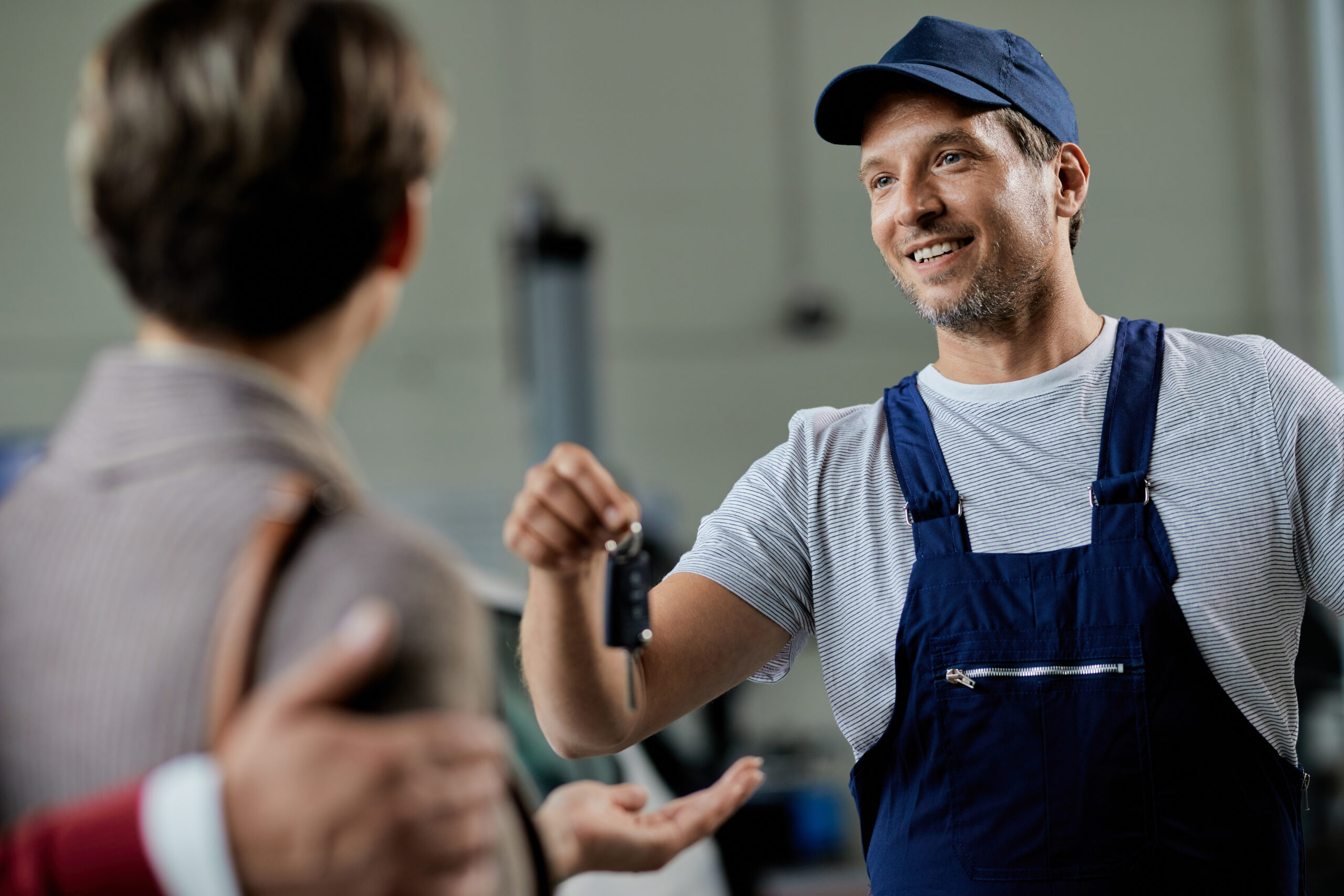 Happy auto repairman handing over cark keys to his customers in a workshop.